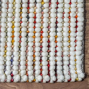 Puede incluir: Primer plano de una alfombra blanca texturizada con rayas de colores. La alfombra está hecha de pequeñas bolas redondas de hilo.