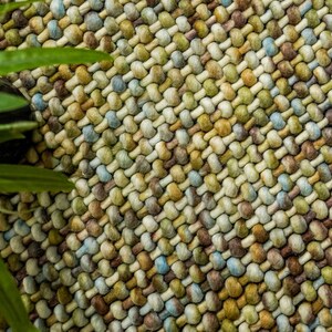 May include: Close-up of a woven rug with a textured surface. The rug is made of a variety of colors, including brown, beige, green, and blue.