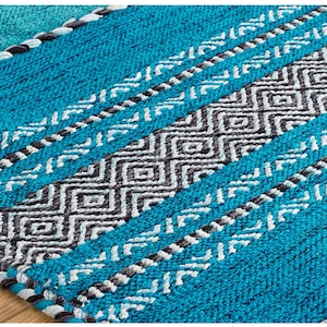 May include: A woven rug featuring a vibrant turquoise blue base with alternating horizontal bands of dark charcoal gray and light gray geometric diamond patterns, accented by thin braided lines of white and dark gray yarn throughout the texture.