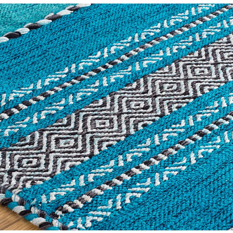 May include: A woven rug featuring a vibrant turquoise blue base with alternating horizontal bands of dark charcoal gray and light gray geometric diamond patterns, accented by thin braided lines of white and dark gray yarn throughout the texture.