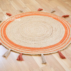 May include: A round jute rug with a natural beige color and orange stripes around the edge. The rug has tassels around the edge in both beige and orange.