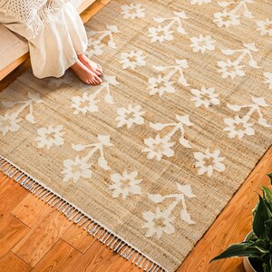 May include: A beige and white area rug with a floral pattern. The rug has a fringe border and is made of natural fibers.