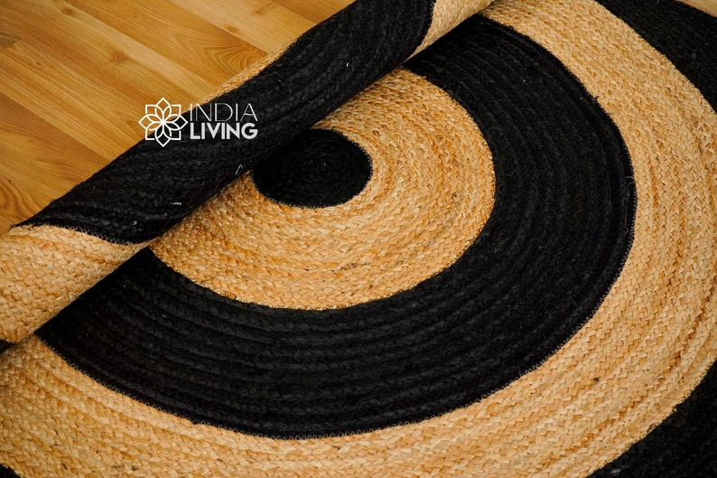 May include: A round jute rug with a black and natural color pattern. The rug has a concentric circle design with a black outer ring and a natural inner ring.