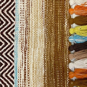 May include: A woven rug with a brown, beige, and blue striped pattern. The rug has a fringe with tassels in various colors, including orange, yellow, blue, brown, and white.