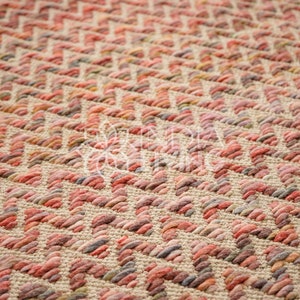 May include: Close-up of a woven rug with a repeating zigzag pattern. The rug features a blend of colors, including beige, red, pink, and gray, creating a textured surface. The design is geometric and visually appealing.