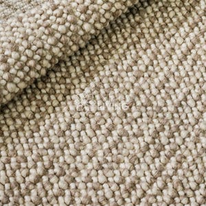 Könnte beinhalten: Nahaufnahme eines strukturierten Teppichs mit einem sich wiederholenden Muster aus kleinen, abgerundeten, beige- und braunen Elementen. Der Teppich hat ein weiches, einladendes Aussehen, mit einer leichten Falte in der oberen linken Ecke. Das Thema ist Inneneinrichtung.