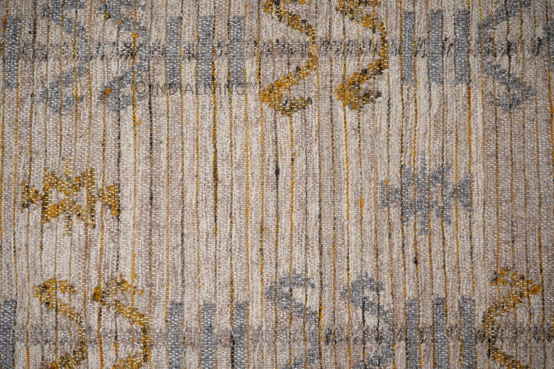 May include: Close-up of a textured fabric with a striped pattern in shades of gray, white, and gold. The fabric has a subtle woven design with small, repeating motifs.
