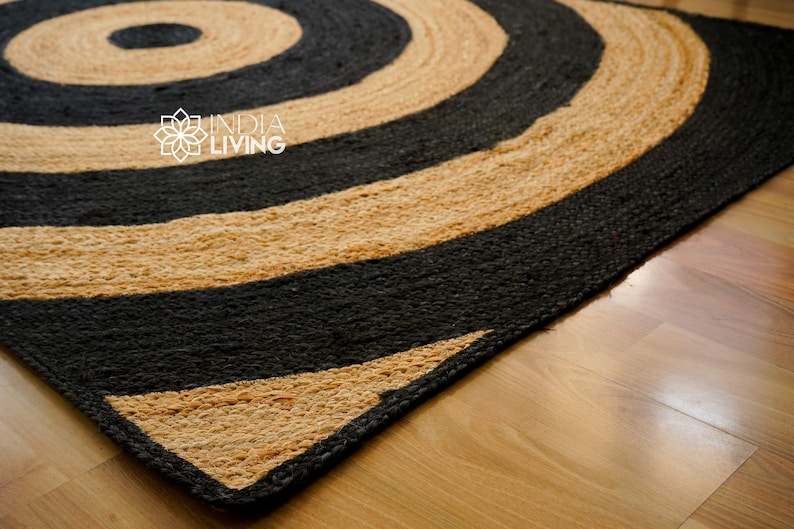 May include: A round jute rug with black and natural colored stripes in a concentric circle pattern. The rug is made of natural fibers and has a rustic look.