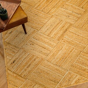 May include: A natural fiber woven rug with a diamond pattern in a light brown color. The rug is made of jute and has a natural, earthy look.