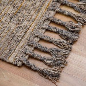 May include: A woven rug with a fringe border. The rug has a light brown and yellow striped pattern.