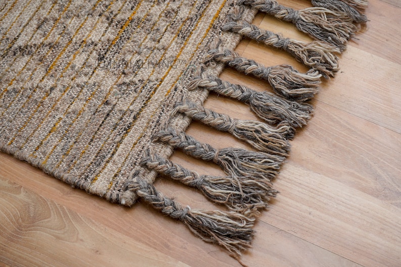May include: A woven rug with a fringe border. The rug has a light brown and yellow striped pattern.