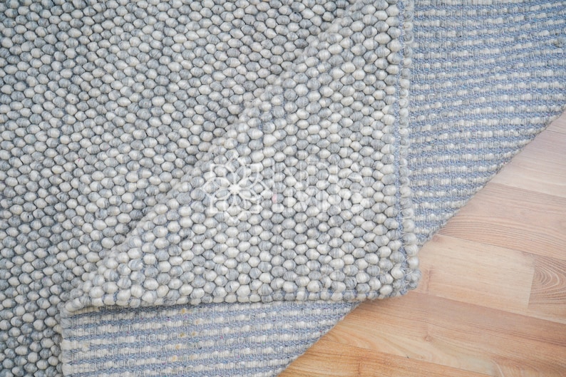 May include: A gray and white wool rug with a textured, bumpy surface. The rug has a striped pattern on the bottom edge.