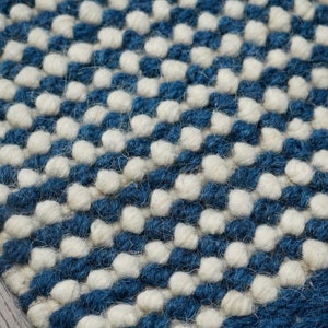 May include: Close-up of a blue and white woven rug with a textured, bumpy surface. The rug is made of wool and has a modern, geometric design.