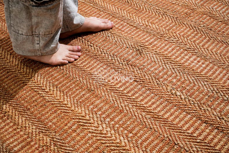 May include: A woven area rug featuring a repeating herringbone pattern in shades of natural tan and burnt orange. The textured surface is constructed from thick, braided fibers, creating a dense and durable floor covering with a distinct zigzag design.