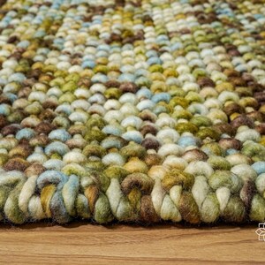 May include: Close-up of a multi-colored woven rug with a textured surface. The rug is made of different shades of brown, green, blue, and white yarn.