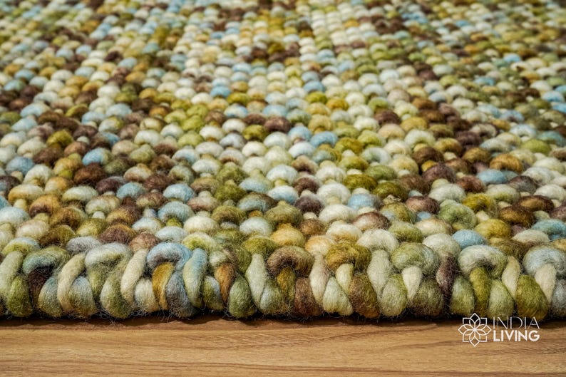 May include: Close-up of a multi-colored woven rug with a textured surface. The rug is made of different shades of brown, green, blue, and white yarn.