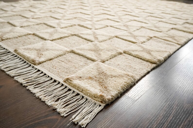 May include: A beige area rug with a geometric pattern and fringe edging. The rug is made of a soft, textured material.