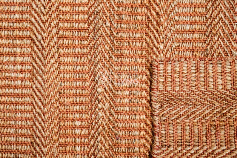 May include: A woven rug featuring a prominent herringbone pattern in alternating shades of burnt orange and natural beige. The texture is coarse and fibrous, with a visible grid-like weave structure throughout the surface of the material.