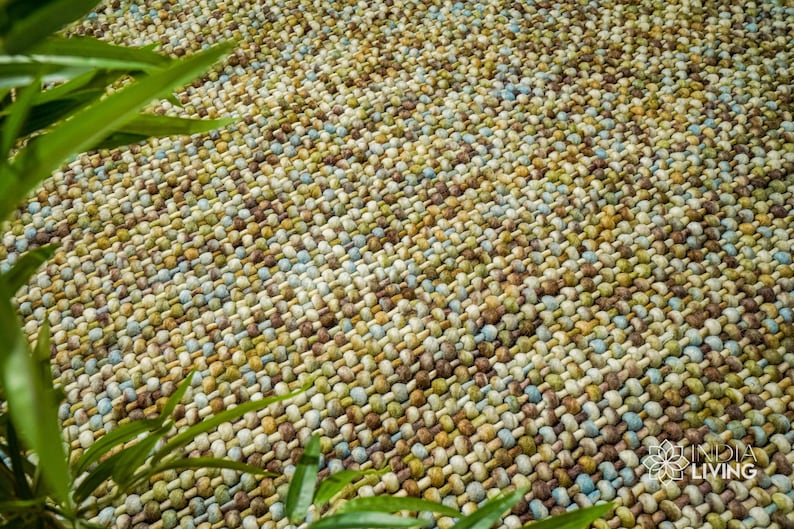 May include: A close-up of a woven rug with a textured surface. The rug is made of small, round, multi-colored beads in shades of brown, green, blue, and white.