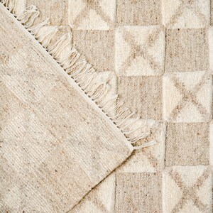 May include: A beige and white woven rug with a geometric pattern. The rug has a fringe border.