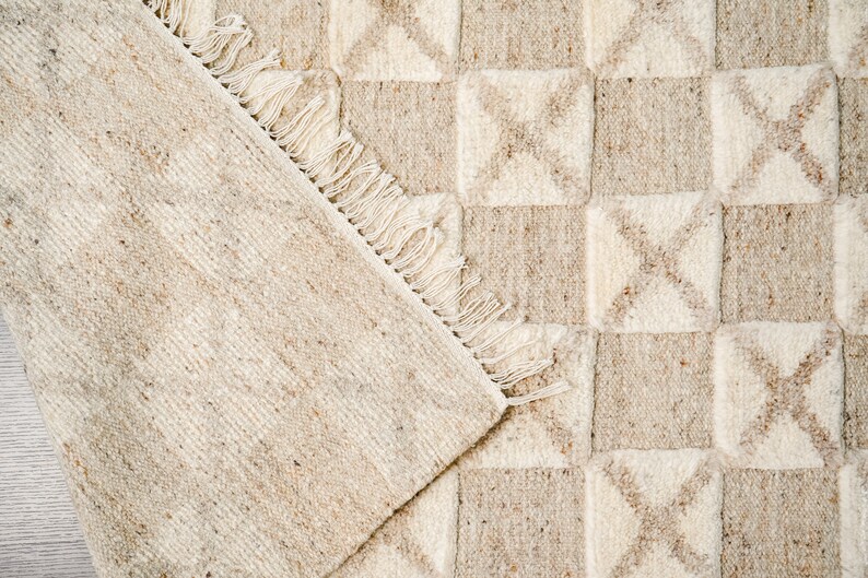 May include: A beige and white woven rug with a geometric pattern. The rug has a fringe border.