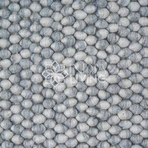 May include: Close-up of a gray and white wool rug with a textured, pebble-like design.