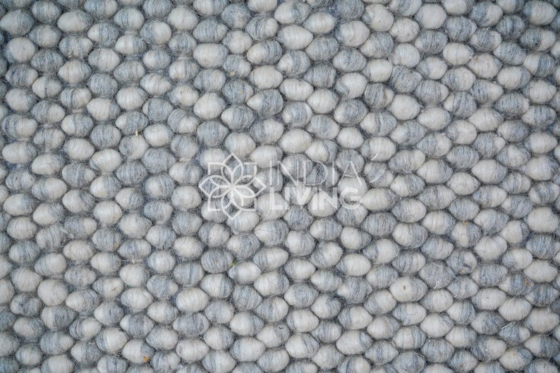 May include: Close-up of a gray and white wool rug with a textured, pebble-like design.