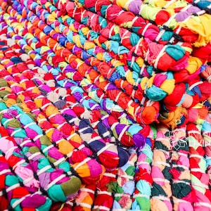 May include: A colourful braided rug made from recycled fabric scraps. The rug is woven in a tight pattern with a variety of colours, including red, blue, green, yellow, and purple.