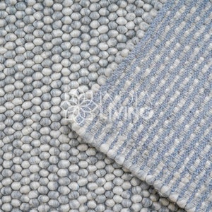 May include: Two different styles of gray and white wool rugs. One rug has a textured, bumpy surface and the other has a striped pattern.