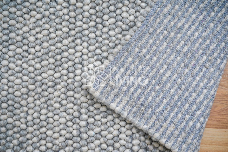 May include: Two different styles of gray and white wool rugs. One rug has a textured, bumpy surface and the other has a striped pattern.