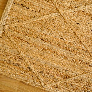 May include: A natural fiber rug with a woven pattern in a light brown color. The rug has a thick, textured surface and a geometric design.