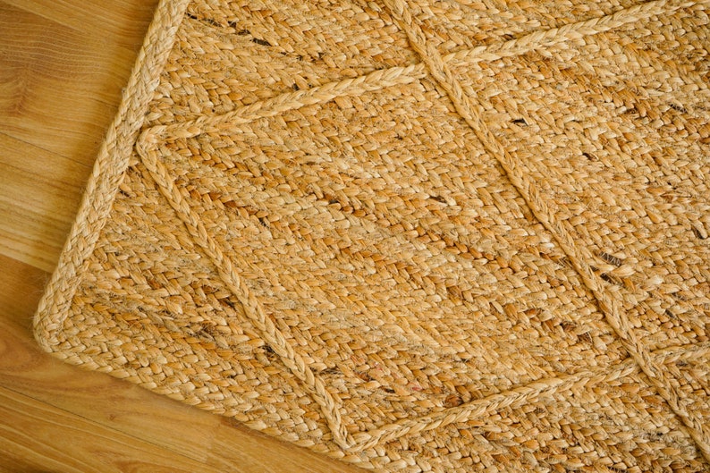 May include: A natural fiber rug with a woven pattern in a light brown color. The rug has a thick, textured surface and a geometric design.