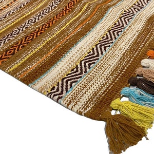 May include: A brown woven rug with colorful tassels. The rug has a geometric pattern with stripes and zigzags.