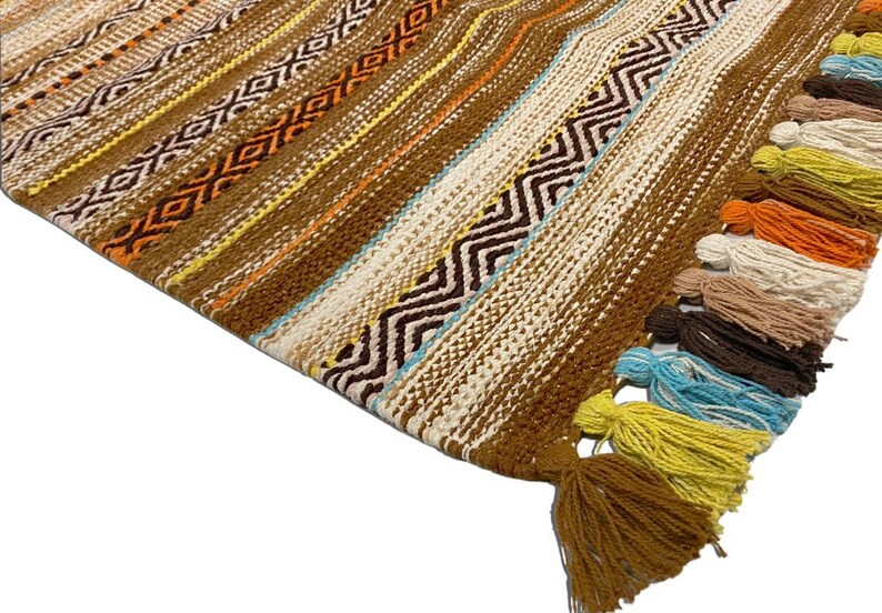 May include: A brown woven rug with colorful tassels. The rug has a geometric pattern with stripes and zigzags.