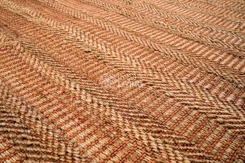 May include: A woven rug featuring a textured herringbone pattern in alternating shades of natural tan and burnt orange. The surface consists of thick, braided fibers arranged in a repeating zigzag design across the entire rectangular area.