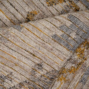 May include: Close-up of a woven fabric with a textured pattern. The fabric is a mix of beige, brown, and gray colors with a subtle yellow stripe.