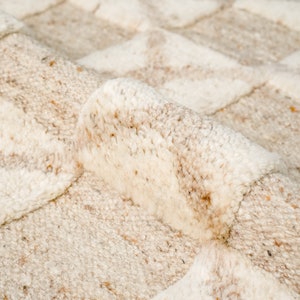 May include: Close-up of a cream-colored rug with a textured, woven pattern. The rug has a soft, fluffy texture and a subtle, light brown color.