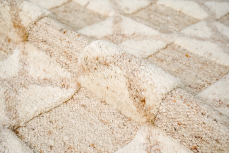 May include: Close-up of a cream-colored rug with a textured, woven pattern. The rug has a soft, fluffy texture and a subtle, light brown color.