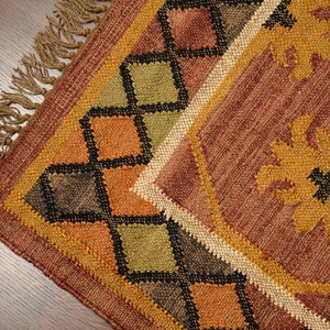 May include: A brown, orange, and green woven rug with a geometric pattern and fringe. The rug has a diamond pattern with black accents.