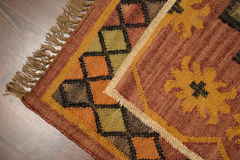 May include: A brown, orange, and green woven rug with a geometric pattern and fringe. The rug has a diamond pattern with black accents.