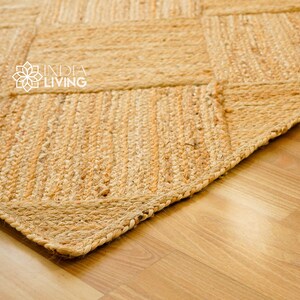May include: Close-up of a natural fiber rug with a woven pattern. The rug is made of jute and has a light brown color. The rug is on a wooden floor.