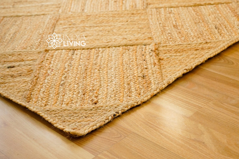 May include: Close-up of a natural fiber rug with a woven pattern. The rug is made of jute and has a light brown color. The rug is on a wooden floor.