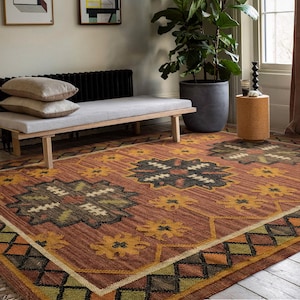May include: A brown and orange patterned rug with a geometric design. The rug has a dark brown center with a lighter brown border. The rug is on a wooden floor.