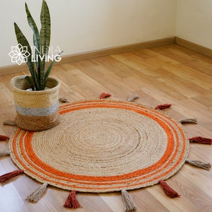 May include: A round jute rug with orange stripes and tassels around the edge. The rug is on a wooden floor and a potted plant is in the background.