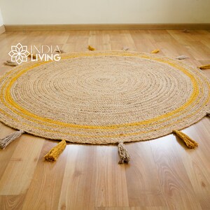 May include: A round jute rug with a yellow stripe around the edge and tassels in yellow and beige. The rug is on a wooden floor.