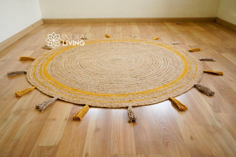 May include: A round jute rug with a yellow stripe around the edge and tassels in yellow and beige. The rug is on a wooden floor.