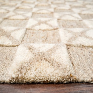 May include: A close-up of a beige and white woven rug with a geometric pattern. The rug has a soft, textured surface and is made of natural fibers.