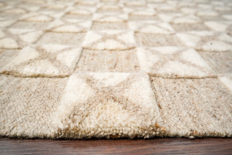 May include: A close-up of a beige and white woven rug with a geometric pattern. The rug has a soft, textured surface and is made of natural fibers.