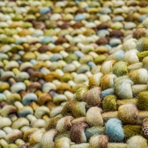 May include: Close-up of a woven rug with a textured surface. The rug is made of a variety of colors, including brown, green, blue, and white.