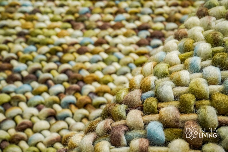 May include: Close-up of a woven rug with a textured surface. The rug is made of a variety of colors, including brown, green, blue, and white.